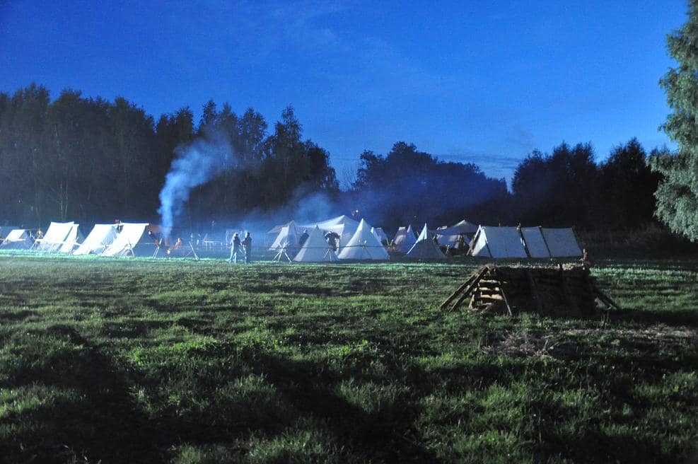 Średniowieczny obóz przed świtem, zasnuty dymem z ognisk.